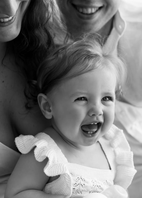 A mother and her laughing toddler cheek to cheek, both mid laugh, in black and white