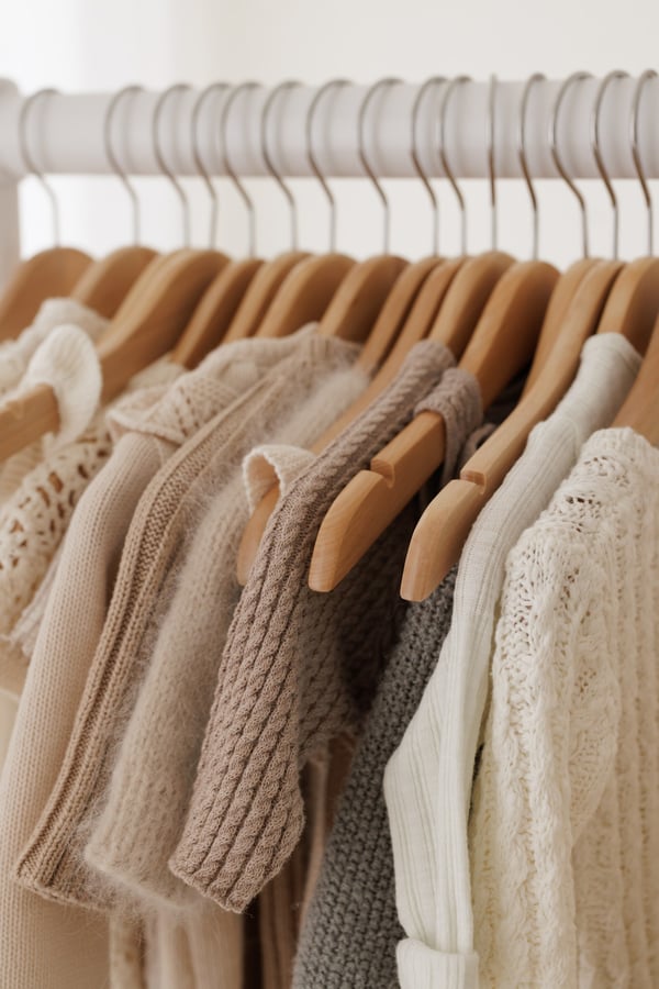A rail of knitted outfits and wraps on wooden hangers, all in cream and soft brown
