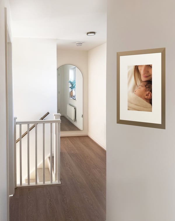 The studio landing: a framed print of a mother cuddling her sleeping newborn on the wall, white banisters and an arched mirror