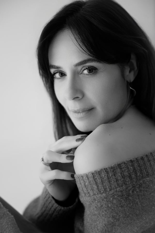 Black and white portrait of the photographer looking over her bare shoulder, hand resting on it, in a soft knitted jumper