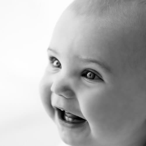 Baby laughing with head tilted back against a white background
