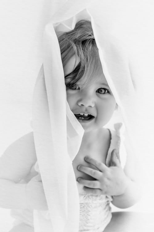 Baby peeking out from under a white cloth, laughing
