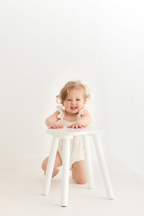 Baby standing and holding on to a small white stool