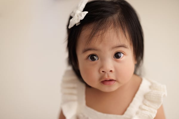 A baby with a small bow in their hair looking straight at the camera
