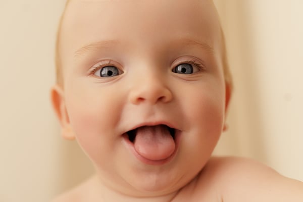 Close portrait of a baby with wide eyes and their tongue out