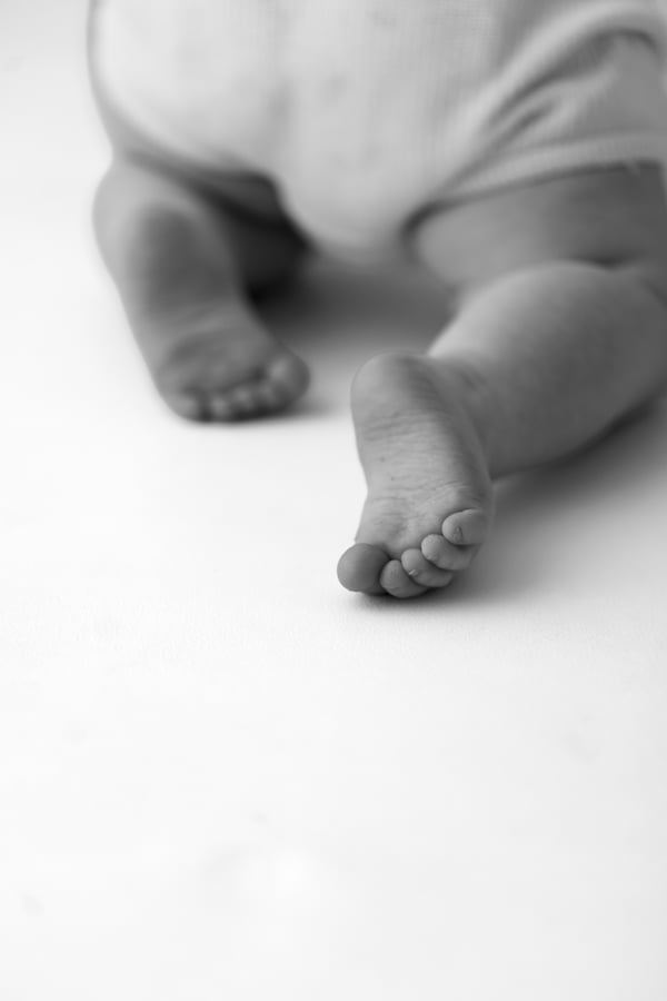 A baby seen from behind on a white backdrop, the soles of both feet in the foreground, in black and white