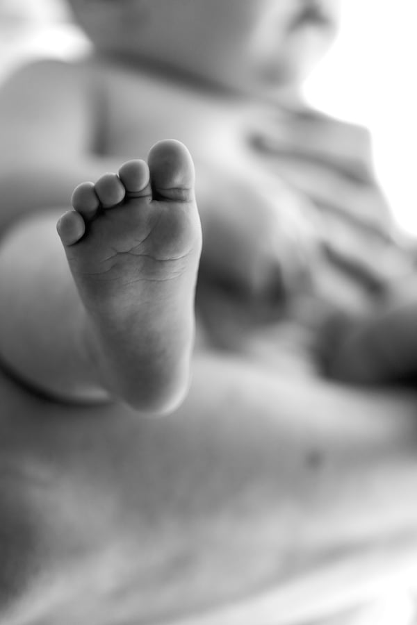 Close view of a baby's foot resting against a parent's hand, in black and white