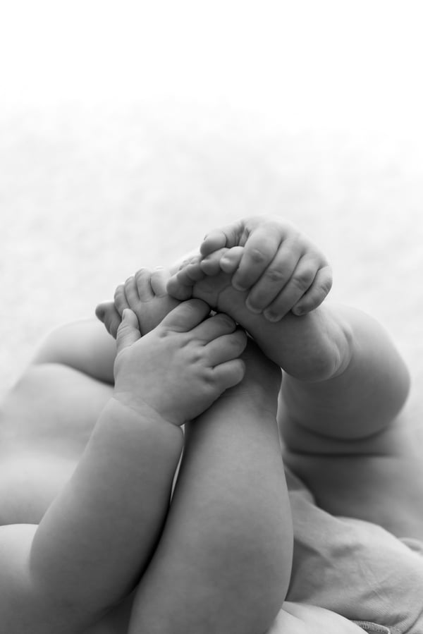 A baby's legs drawn up with both hands holding on, close in, in black and white