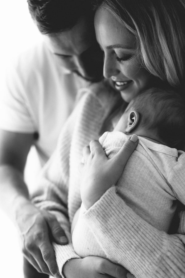 Both parents looking down at their swaddled newborn held between them, in black and white
