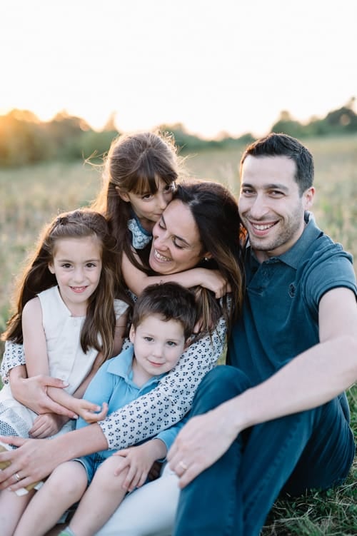Francesca with her husband and their three children, sitting together in a field at golden hour