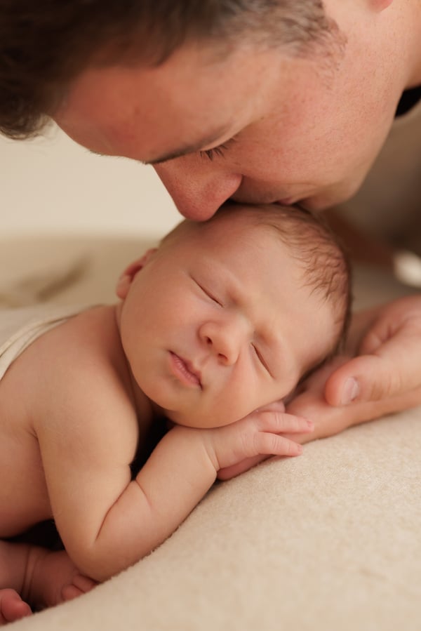 A father leaning down to kiss his sleeping newborn's head