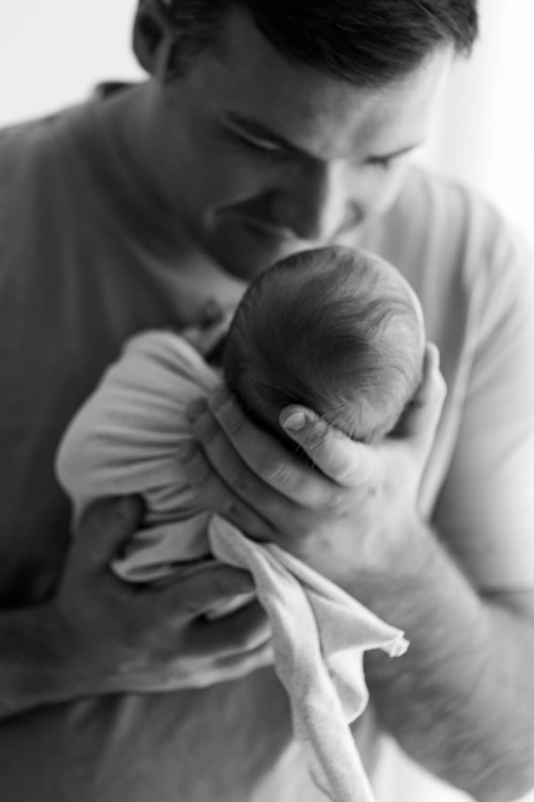 A father smiling down at his newborn held in both arms, in black and white