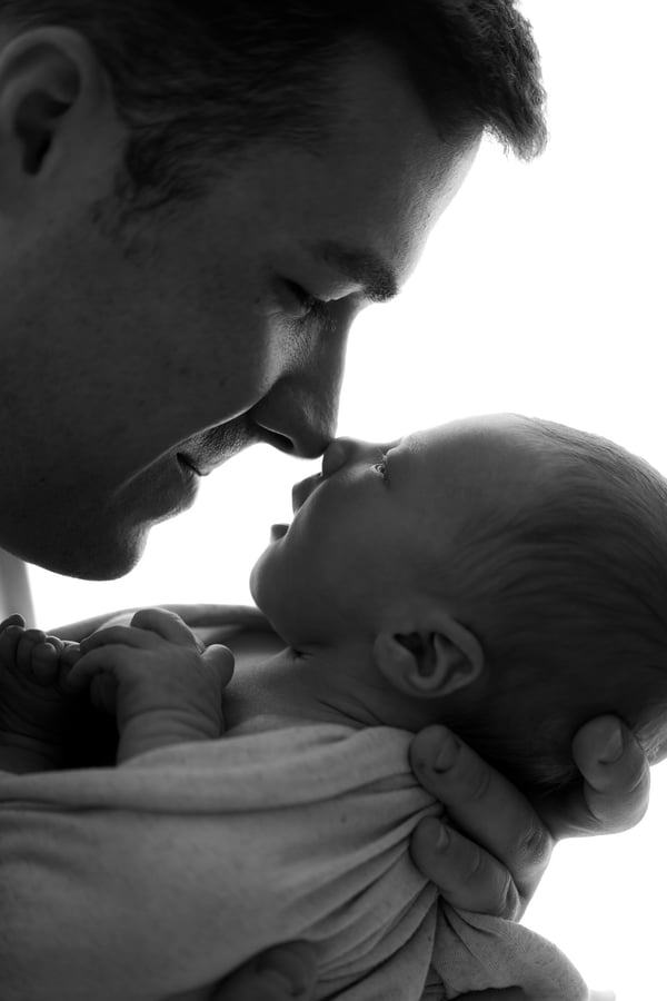 A father leaning nose to nose with his newborn held in his arms, in black and white