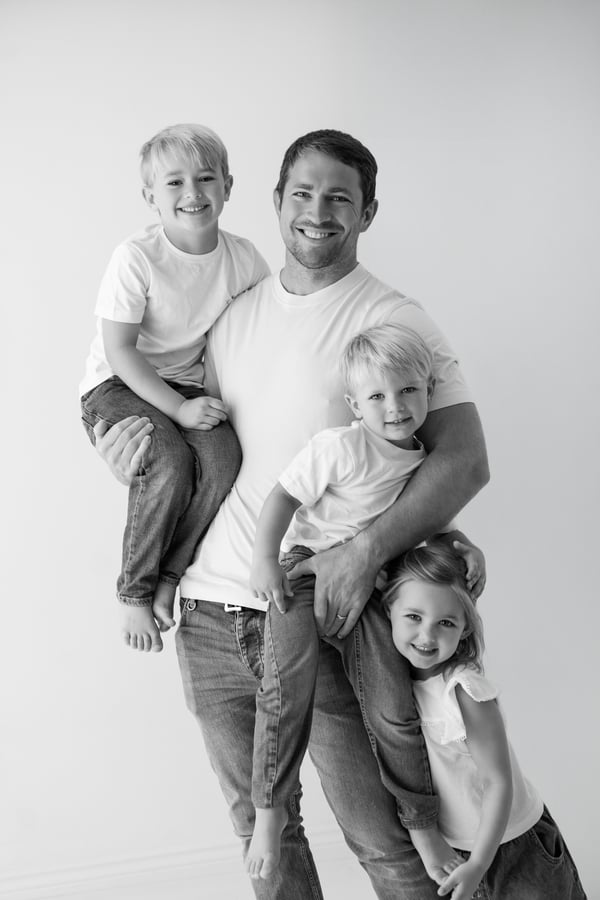 A father holding his three children in the studio, one up on his shoulder, in black and white