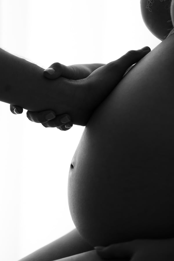 Backlit profile of a seated pregnant belly with a hand resting on it, in black and white