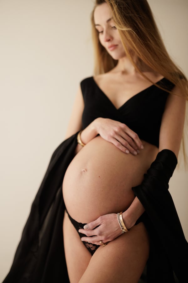 An expectant mother in a black gown open over her bare bump, looking down