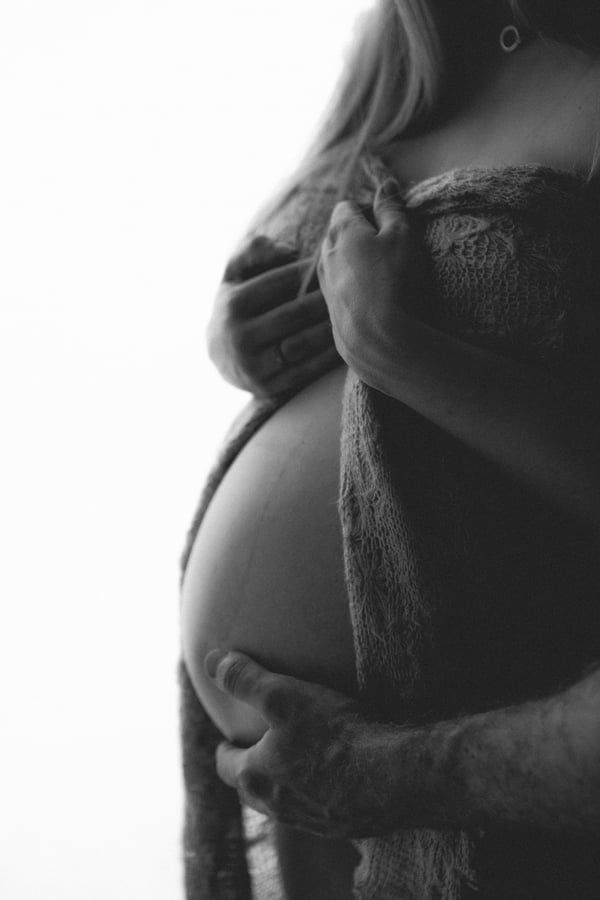 Side profile of a pregnant belly held from underneath, in black and white