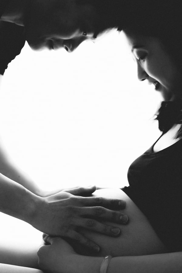 A couple in silhouette against a bright light, hands resting on her bump, in black and white