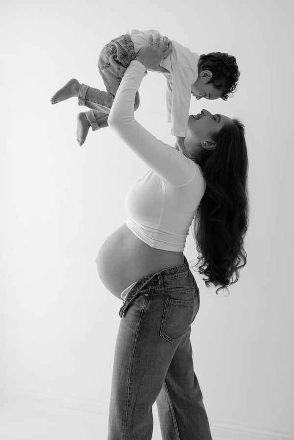 An expectant mother in jeans lifting her young child above her head, in black and white