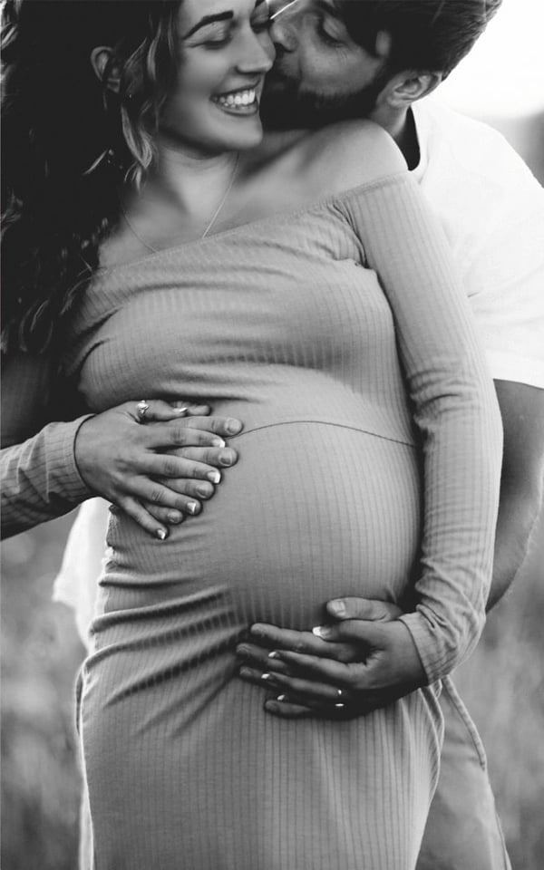 Expectant couple outdoors, her ribbed dress close-fitting, their hands together on the bump