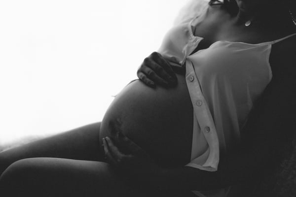 An expectant mother reclining with an open shirt draped over her bump, in black and white