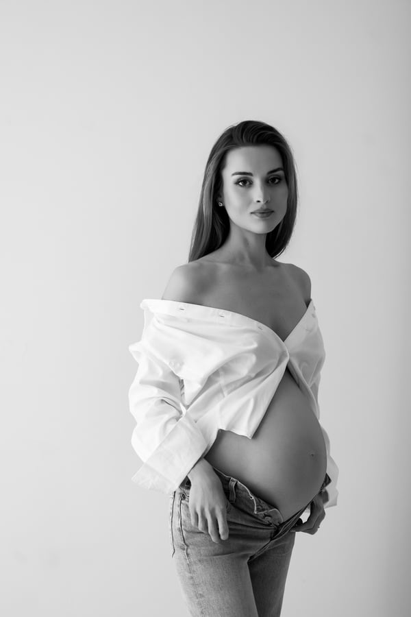 An expectant mother in an open white shirt and jeans, looking towards the camera, in black and white