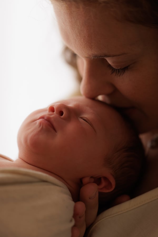 A mother kissing her newborn's forehead, the baby asleep in her arms