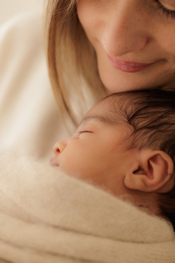 A mother looking down at her newborn, asleep in a beige wrap