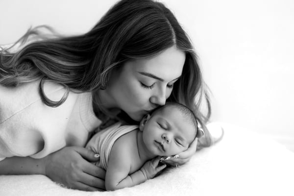 A mother lying down and kissing her newborn's head, in black and white