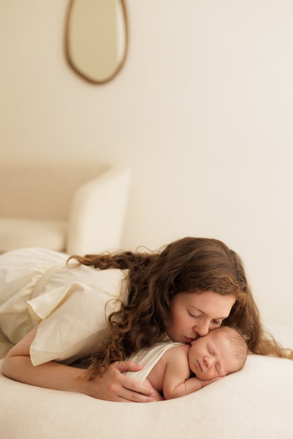 A mother lying down and kissing her newborn, the studio room visible behind