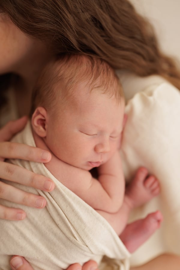 A newborn asleep in a cream wrap, held in their mother's arms
