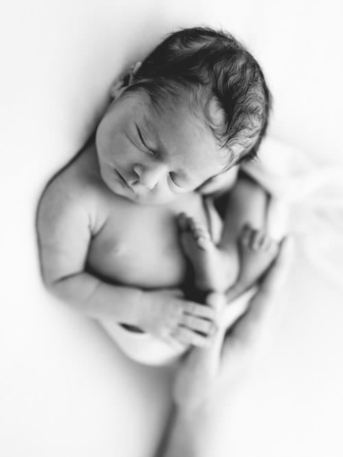 Newborn curled on one side with both hands held together at the chin