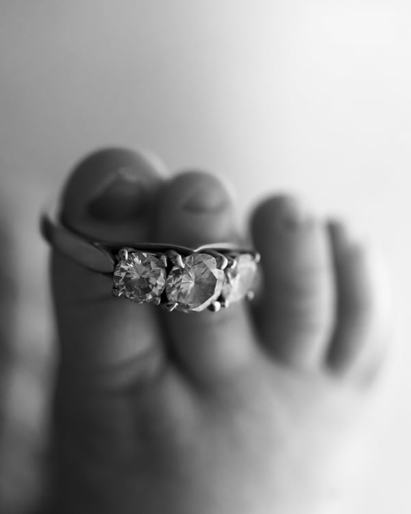 A newborn's feet resting against a hand wearing a diamond ring, in black and white