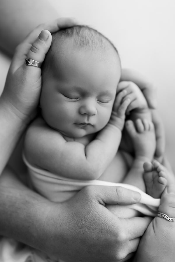 A newborn held upright in a parent's hands, knees tucked in, in black and white