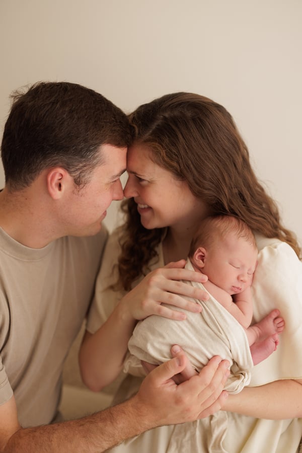 Both parents forehead to forehead, holding their sleeping newborn between them