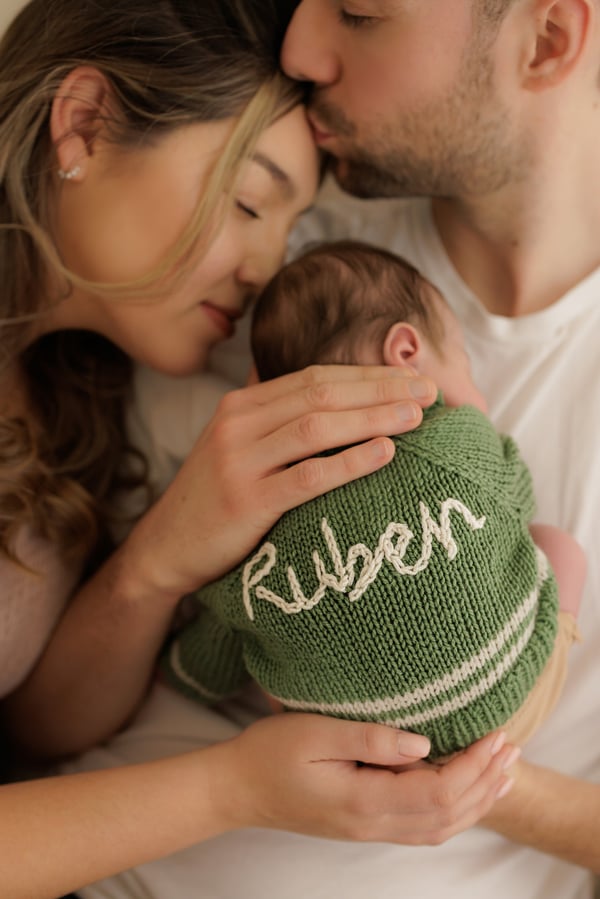 Both parents holding their newborn, who is wearing a green knitted jumper