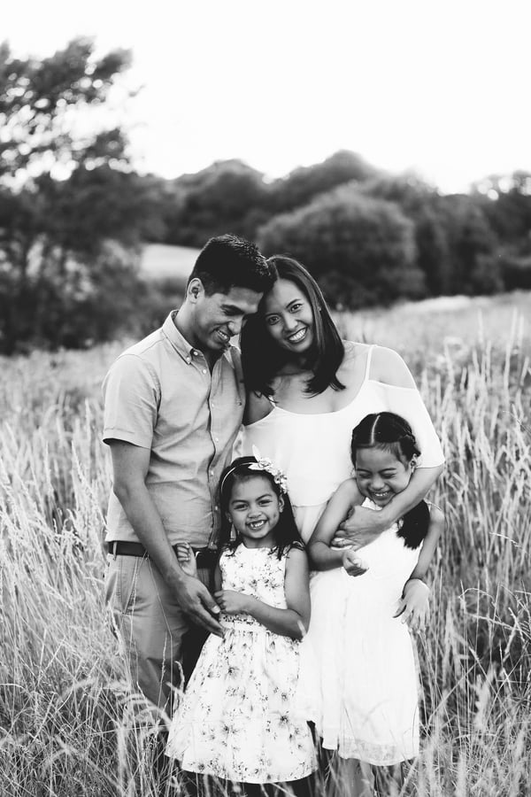 Both parents smiling at each other in a summer field while their three children hold on to them, in black and white