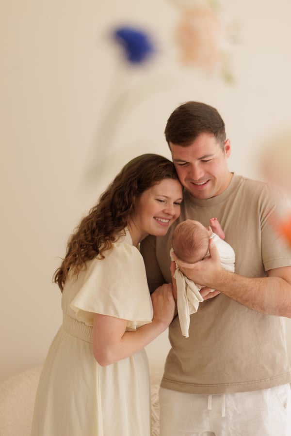 Both parents standing together in the studio, holding their swaddled newborn