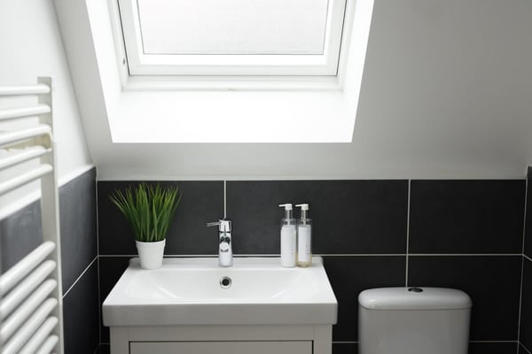 The studio bathroom: a white basin under a skylight, against charcoal tiles