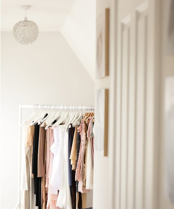 Rail of maternity dresses and fabrics in cream, blush and black, under a woven pendant light