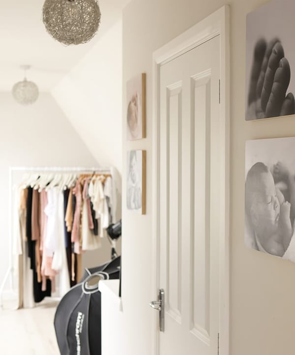 Corner of the studio with a rail of dresses, framed newborn prints on the wall and a door to a separate changing room
