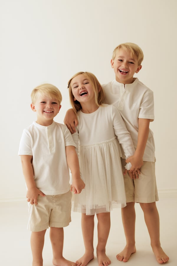 Three children standing together and laughing in the studio, dressed in cream
